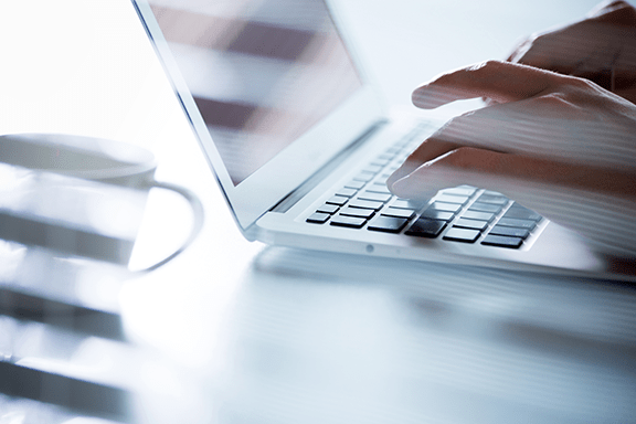 User typing on a laptop with a coffee mug near by