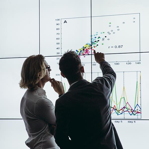 Two researchers analyze data visualizations on a large display screen. 