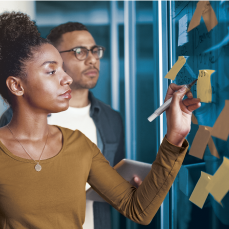 people gesturing toward wall of post-it notes